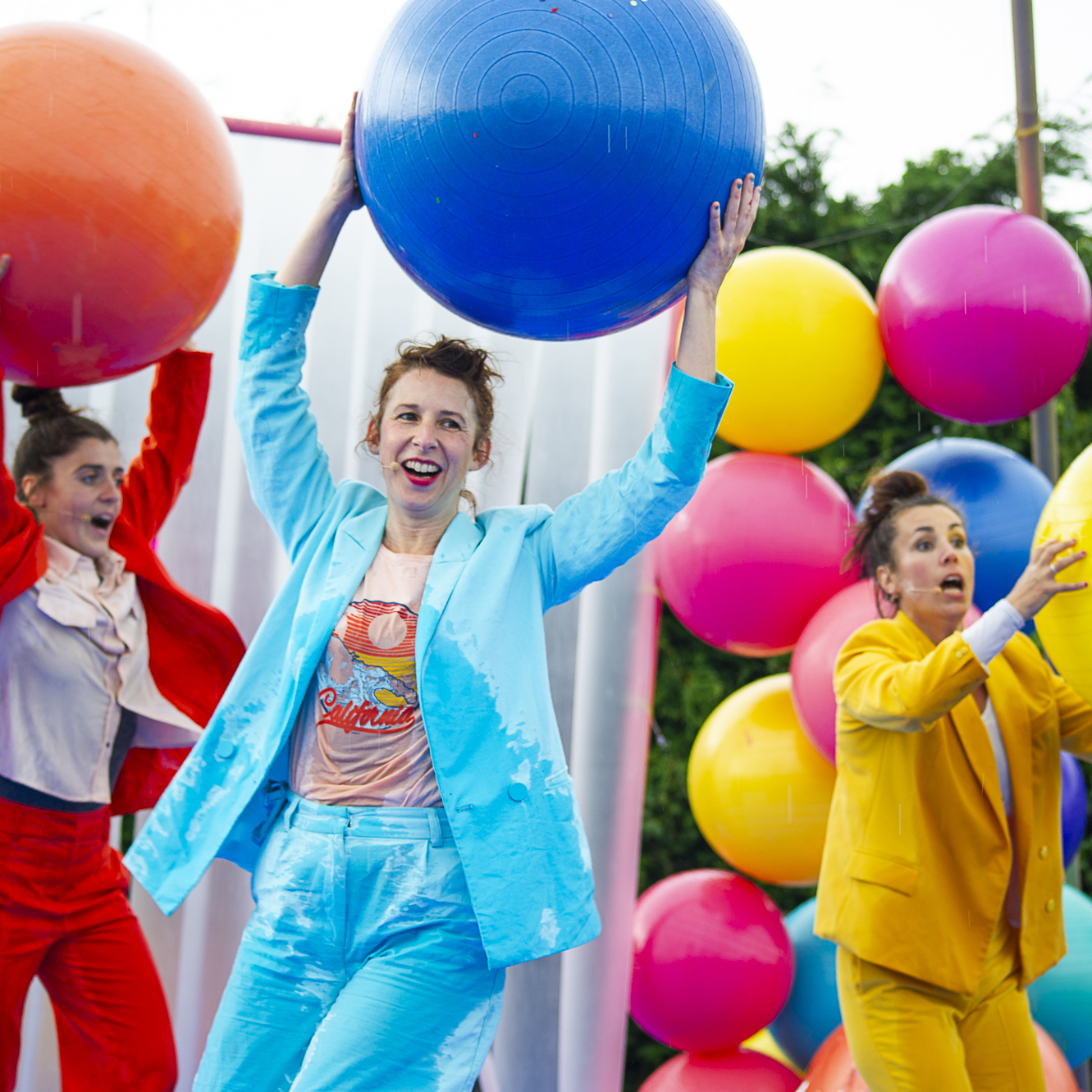 Les 3 artistes portent leur costume de l'émission Bonjour Bonheur, bleu ciel, jaune et orange. Elles sourient en tenant dans leurs mains des ballons de yoga aux couleurs de leurs costumes.